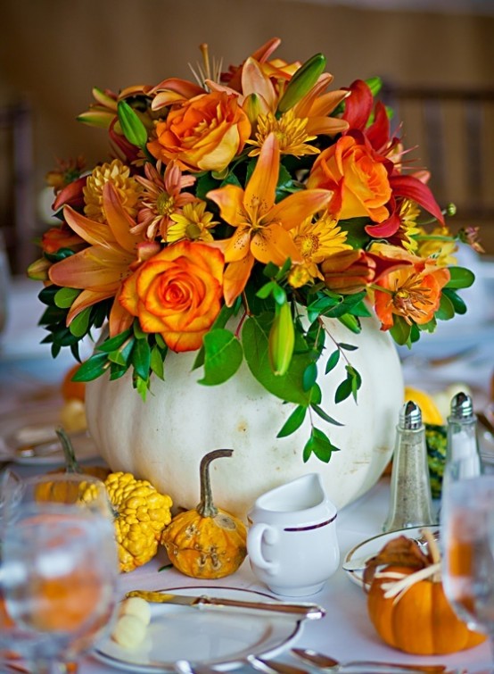an oversized white pumpkin as a vase with orange and red blooms and greenery is a cool and bold fall centerpiece