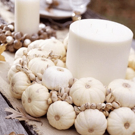 an oversized white pillar candle surrounded with white pumpkins and pistachios is a neutral and chic fall centerpiece