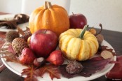 a white plate with bright fall leaves, nuts and acorns and apples and pumpkins for a rustic fall centerpiece