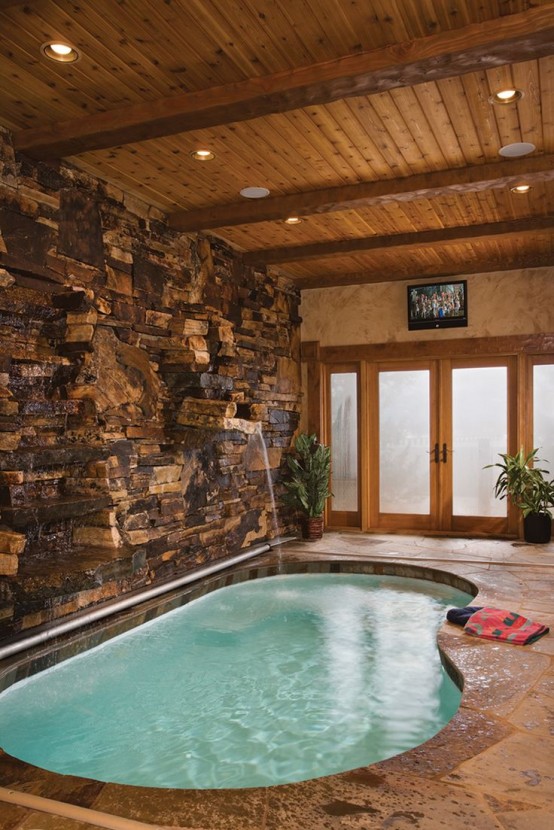 a nature-inspired space with a faux stone wall, a stone deck, a kidney-shaped pool with a waterfall is super relaxing