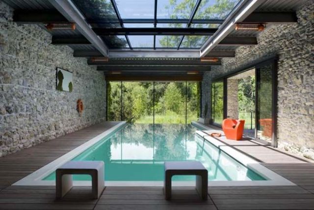 a pavilion with a glass roof and stone walls, a large infinity pool, stools and an orange chair is a lovely space to swim and enjoy the views