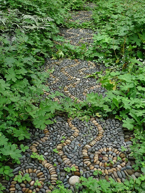 a pebble garden path with black and neutral pebbles with a swirl pattern and curves