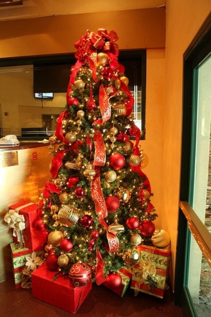 a Christmas tree decorated with red and gold ornaments, ribbons and gift boxes plus bows on top