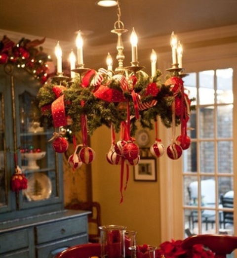 a Christmas chandelier of evergreens, red and white ornaments on red ribbons and gold candleholders