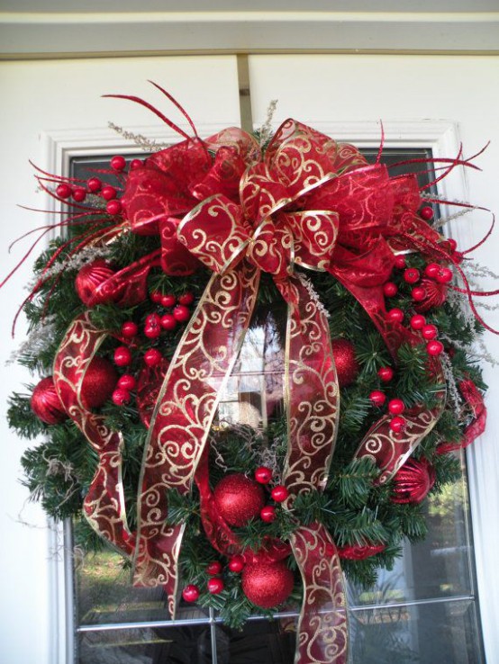 an evergreen wreath with red ornaments of various sizes and red and red and gold ribbons and bows
