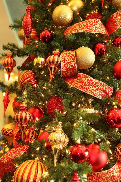 a Christmas tree decorated in red and gold ornaments, with lights, ribbons and lots of glitter