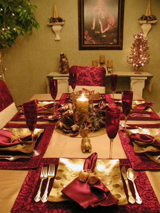 a traditional and glam red and gold Christmas table setting with napkins, gold chargers and cutlery and a bow and candle centerpiece