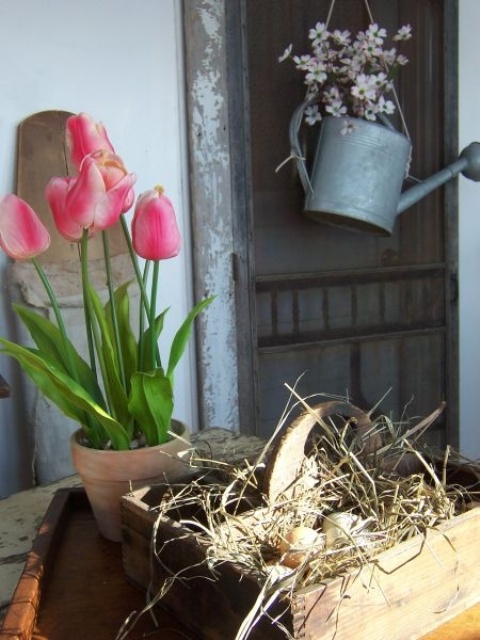 potted pink tulips, fake blooms in a watering can and a box with fake eggs for Easter