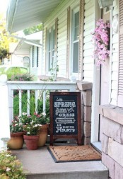 a wreath of faux pink blooms, potted flowers and a chalkboard sign for a natural spring porch