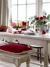a relaxed Christmas tablescape with a bold red floral centerpiece with greenery, a candle arrangement with berries, neutral porcelain and vintage ornaments
