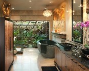 a refined tropical bathroom with an outdoor shower with greenery, a stone tub, gorgeous artworks and a crystal chandelier