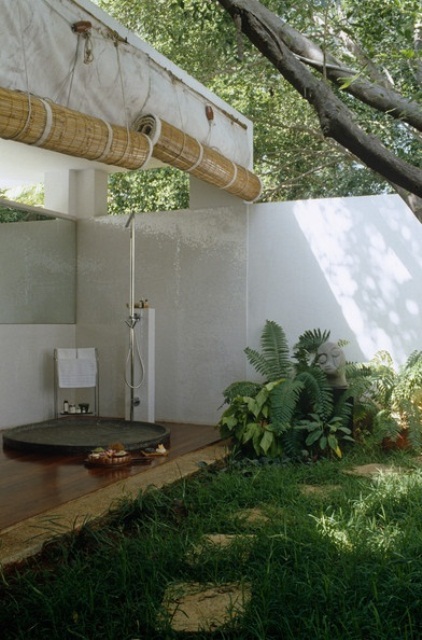 a tropical partly outdoor bathroom with lots of greenery and plants, a shower under a roof and shades that can be opened to outdoors
