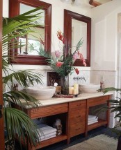 a lush tropical bathroom in neutrals, with a stained vanity, agate sinks and dark stained framed mirrors and potted greenery and blooms