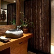 an Asian tropical bathroom with a weathered wood wall, a bamboo space divider, a rough stone sink and some pretty decor