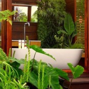 a stained wooden indoor-outdoor bathroom with lots of potted and growing plants, with a tub and floating wooden sinks