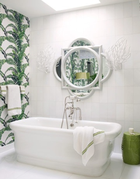 a white tropical bathroom with a tropical leaf accent wall, a white tub and a catchy mirror over it
