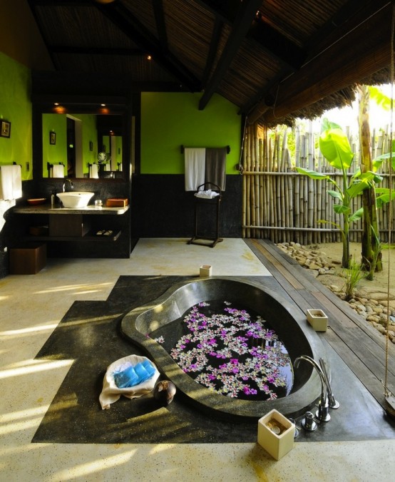 a bright indoor-outdoor bathroom with green and black walls, a sunken stone tub with a view to outdoors and a glass wall that can be removed