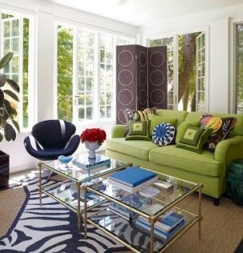 a colorful living room wiht white walls, a green sofa, layered rugs including a faux zebra rug, glass coffee tables and colorful pillows is amazing