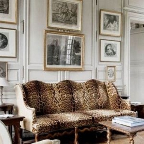 a neutral living room with paneling, a leopard print vintage sofa, vintage carved tables and a large black and white gallery wall for a refined feel