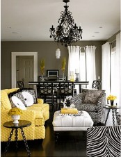 a taupe living room with a bold yellow sofa, zebra print chairs, a white ottoman and a black chandelier for a bolder and catchier look