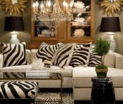 an elegant art deco living room with a white sectional, zebra print pillows, a glass cabinet for storage and a crystal chandelier plus black lamps