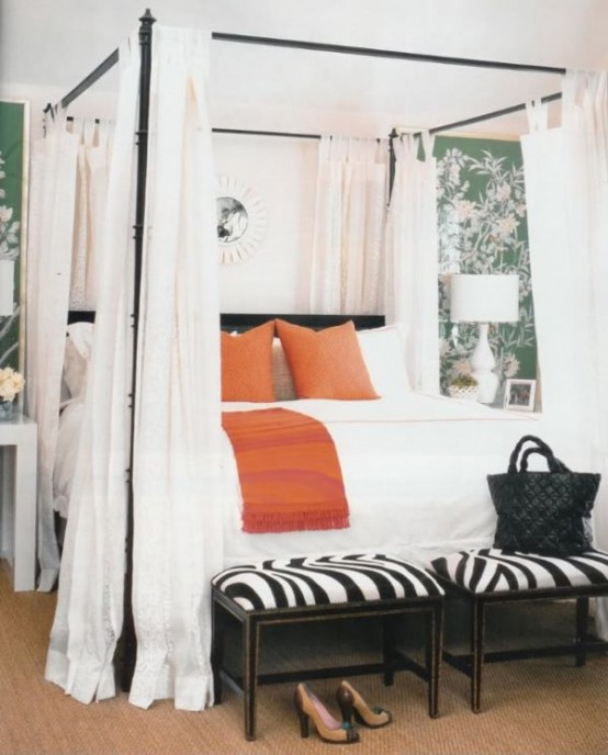 a stylish bedroom with green botanical print walls, a canopy bed with white curtains, orange and white pillows and zebra print stools at the foot of the bed