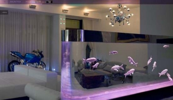 a minimalist and refined living room done in white, with chic furniture, a chic chandelier and a sheer aquarium that takes one wall