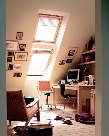 a small attic home office with a skylight, a desk, a chair and some stools, built-in shelves and a cool gallery wall on two walls is cool