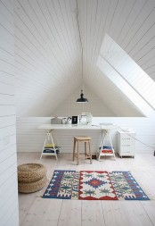 a clean white attic home office with planked walls and a ceiling, two windows, a trestle desk, a stool and a printed rug for a bold touch