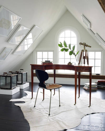 an elegant attic home office with white windows, gallery walls, a stained vintage desk, a wooden chair and some glass storage units