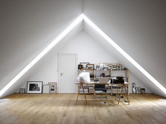 a small attic home office with a creative skylight, a trestl desk and a leather chair, a wooden shelving unit, artworks right on the floor