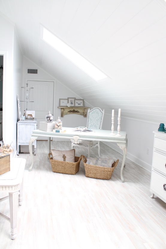 a white attic home office with a skylight, a refined desk and a vintahe chair, beautiful storage units, baskets and a small gallery wall on a shelf