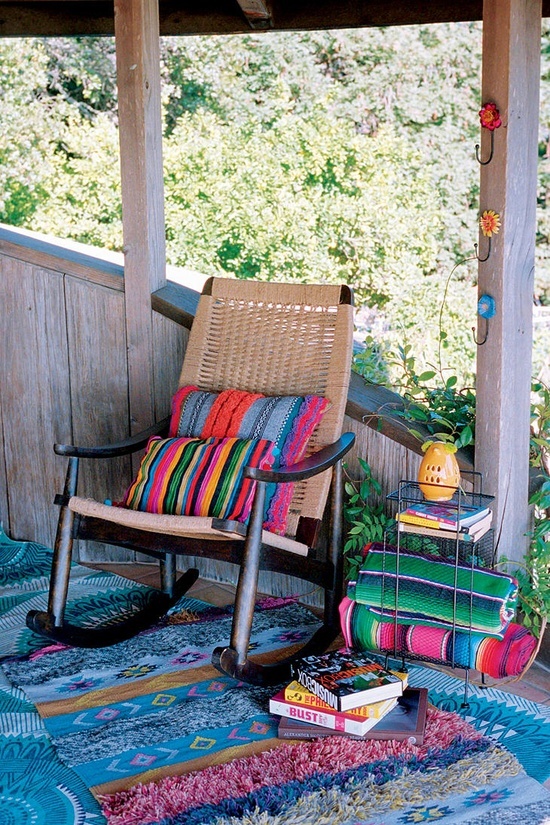 a colorful boho porch with bright printed textiles, a woven chair and colorful books stacked