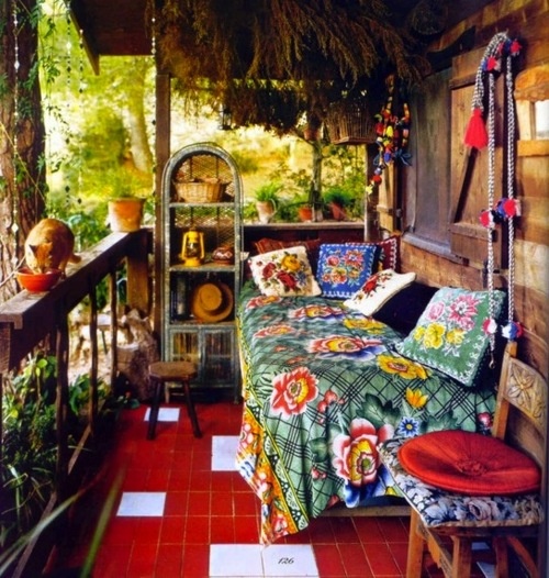 a super colorful boho porch with a relaxing nook   a daybed with colorful and printed floral textiles, a a woven storage unit, colorful furniture and greenery in pots