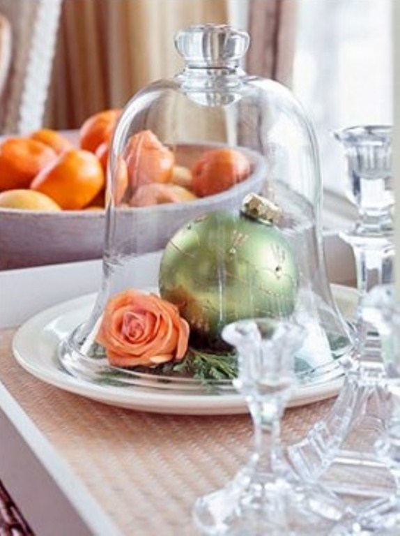 a chic glass cloche with a large green Christmas ornament and a bloom is an elegant holiday centerpiece
