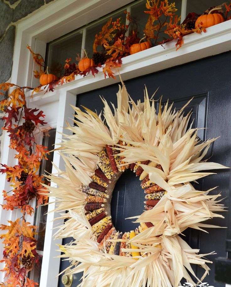rustic fall door decor with a corn cob and husk wreath and bright faux leaves and pumpkins framing the door is fun and cool