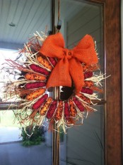 a bright rustic fall wreath made of corn cobs and corn husks and topped with an orange burlap bow with a button is a fantastic idea