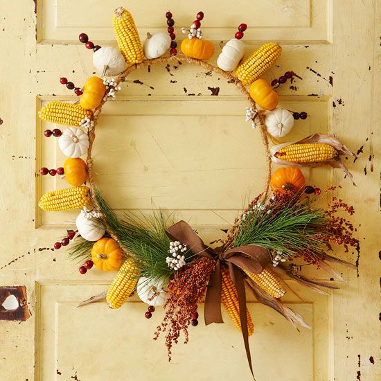 a bright rustic fall wreath made of yellow and white pumpkins and gourds, corn cobs, cranberries, greenery and berries plus a ribbon bow