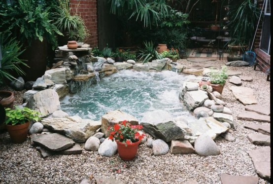 Beautiful in-ground natural-looking stone hot tub  surrounded by pebbles.