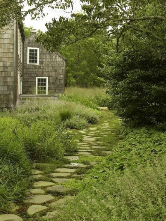 a nautral rough stone gardne pathway with greenery growing in between the rocks looks relaxing and calming and matches the greenery