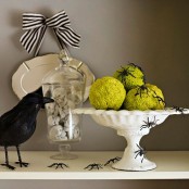 a Halloween console table with a plate with a striped bow, a bowl with pea balls, spiders and a blackbird