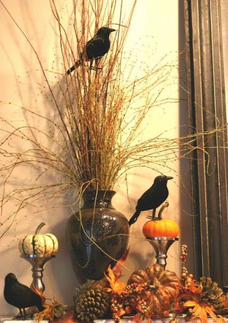 stylish Hallowene decor with a vase with branches, faux pumpkins, pinecones and leaves, blackbirds, stands with pumpkins