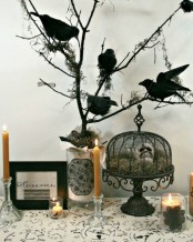 a Halloween console table styled with a sign, a cage stand with hay and a skull, branches and blackbirds and some candles