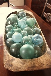 a large dough bowl with blue glass floats is a cool centerpiece for a coastal home