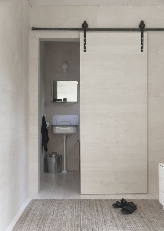 a white plywood sliding door hides the bathroom and saves space