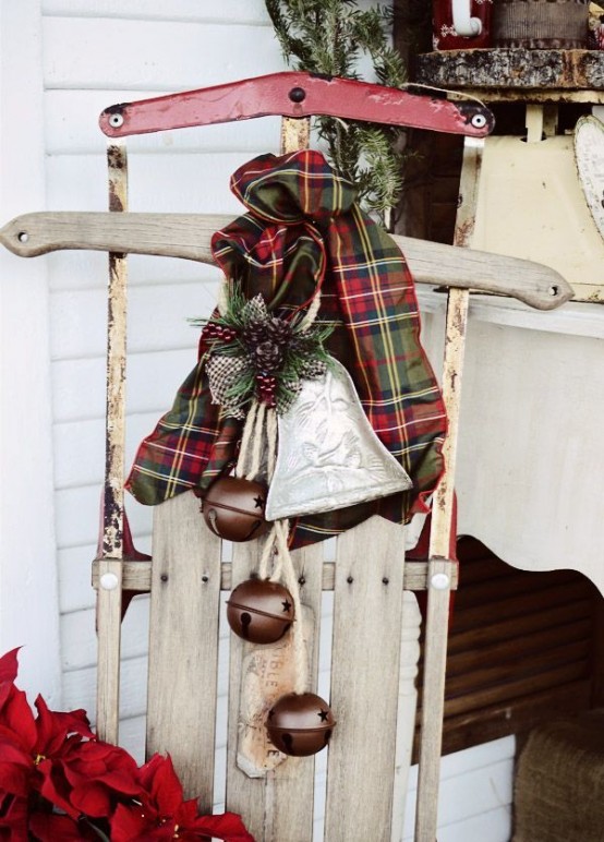 a vintage wooden sledge with a plaid scarf, a porcelain bell ornament and some large brown bells for outdoor decor