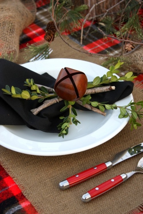 a natural Christmas place setting with a black napkin accented with sticks, greenery and an oversized bell for a rustic Christmas tablescape