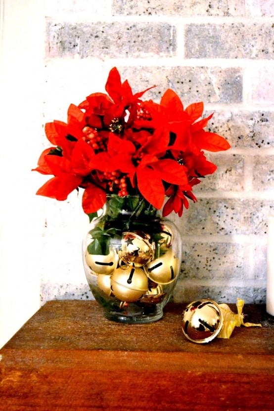 a sheer glass vase with gold bells and faux poinsettia and berries is a lovely and bold Christmas centerpiece