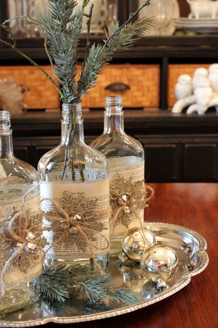 a vintage rustic Christmas centerpiece of a silver tray with fir twigs and silver ornaments, bottles with snowflakes and silver bells and fir twigs in them