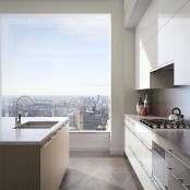 a beautiful contemporary kitchen with sleek plain white cabinets, stone countertops and a wood backsplash, a light-stained kitchen island with a white sotne countertop and a gorgeous view of the big city